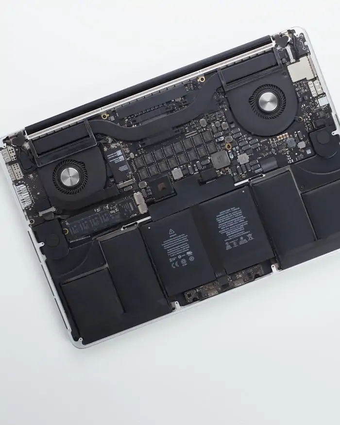 An opened laptop with its back cover removed, exposing the logic board, battery and cooling fans.
